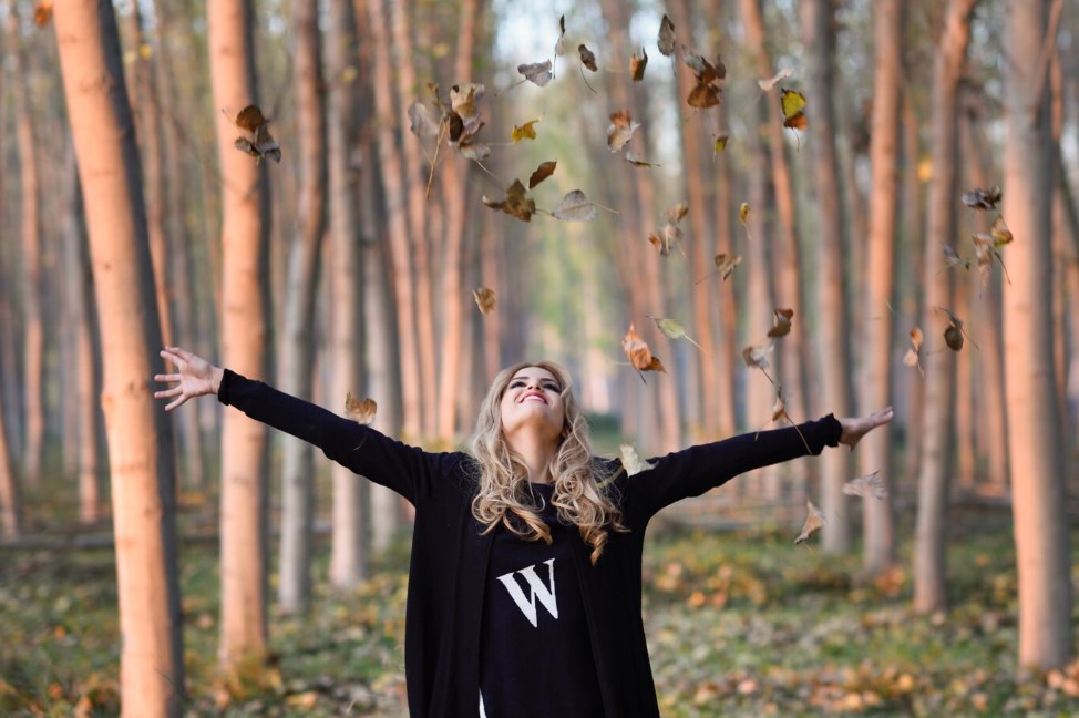 a young woman throwing leaves in the air in the forest