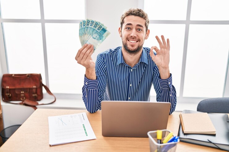 a young man sitting in a modern office, smiling and holding a wad of money in his hand