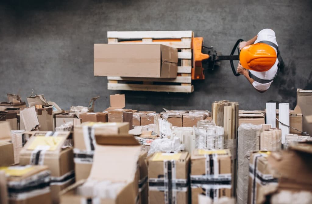 A worker in a safety helmet operating a forklift in a cluttered warehouse