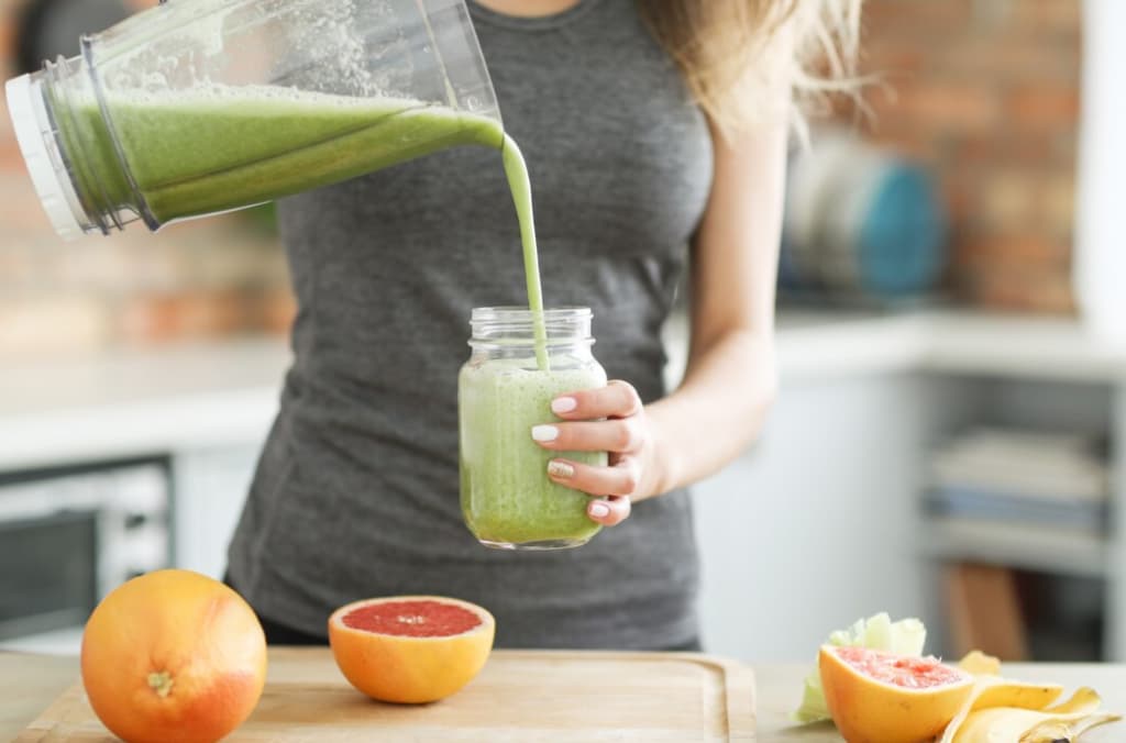 Person pouring a green smoothie into a jar next to fresh fruits