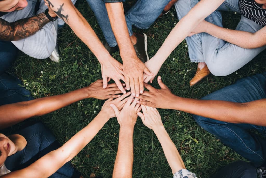 Diverse hands coming together in a circle over grass, symbolizing unity