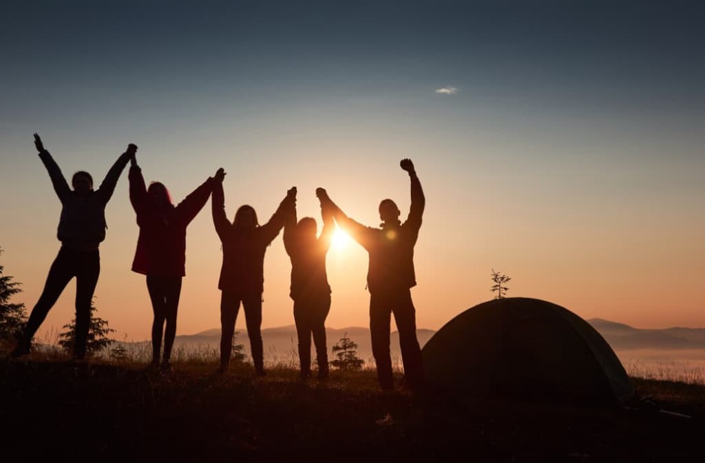 Silhouettes of people with arms raised in triumph beside a tent at sunrise