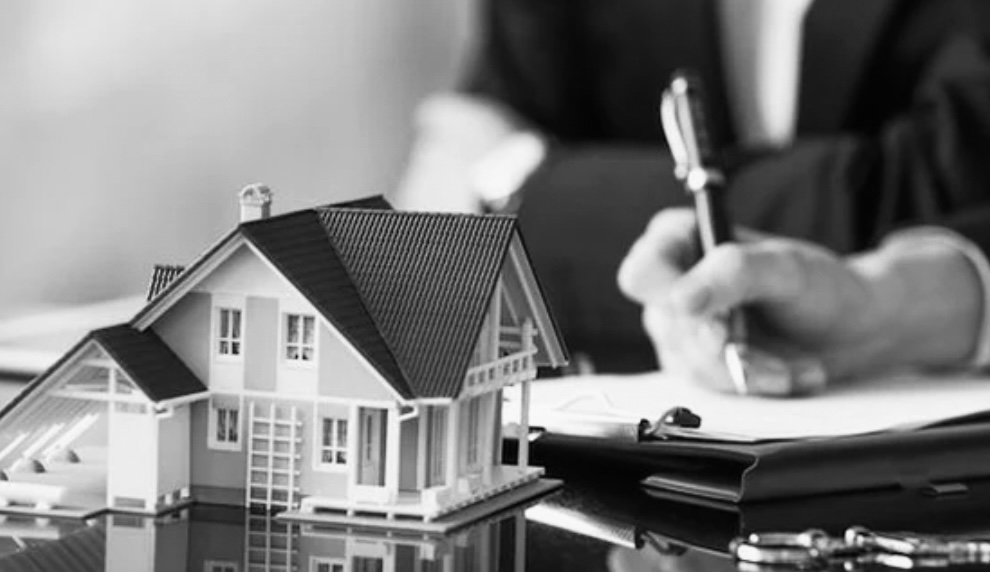 A grayscale image of a scaled model of a two-story house with a pitched roof, placed on a reflective surface